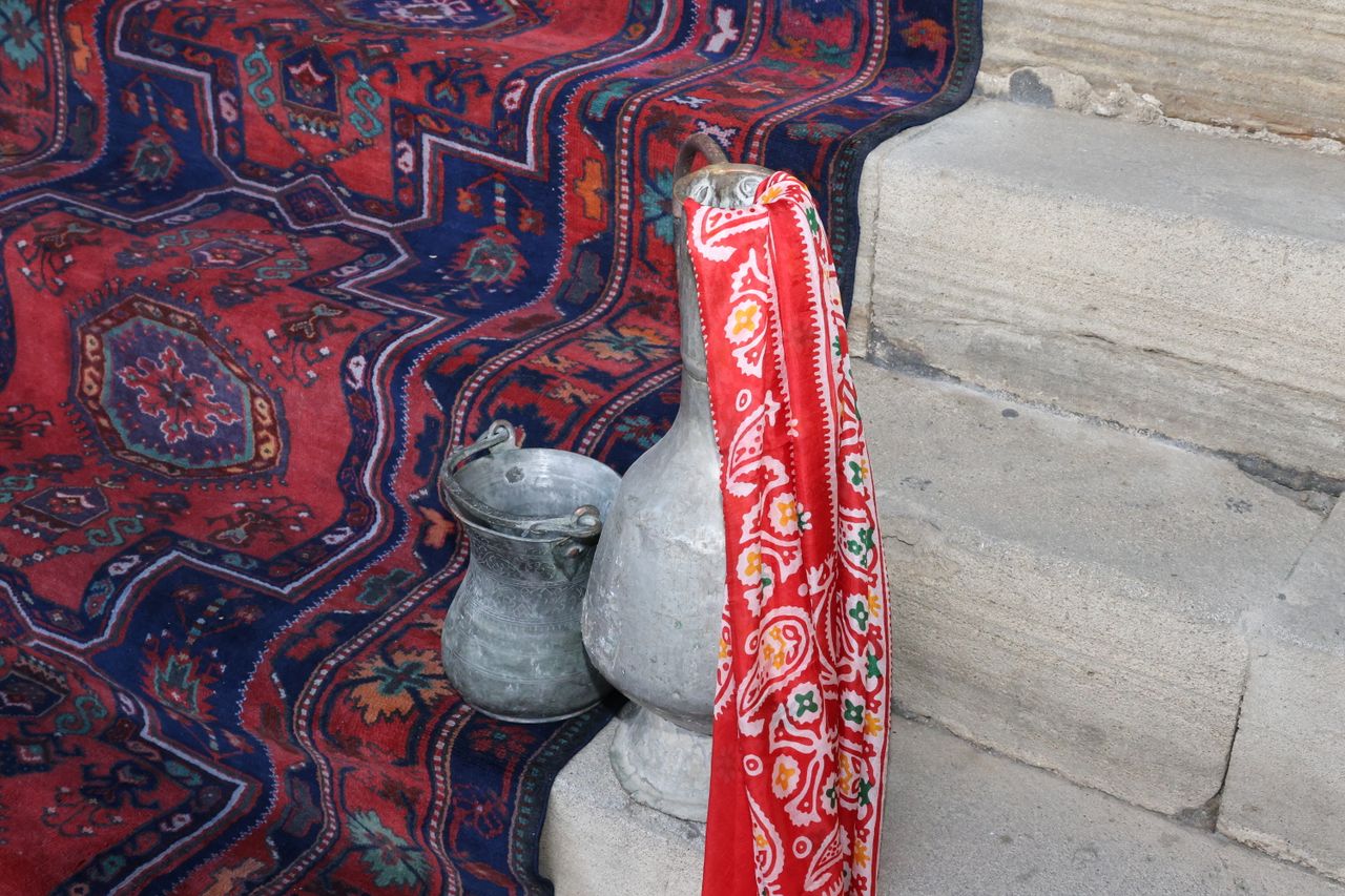 Intricate textile with metal jugs on stone steps creating a traditional and vibrant scene.